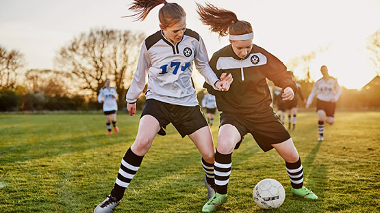 Two female student athletes playing soccer.