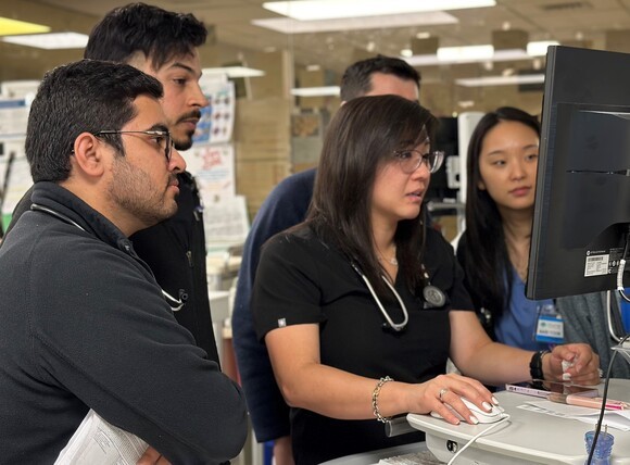 Several pulmonary and critical care medicine fellows huddle around a monitor to review and discuss imaging results.