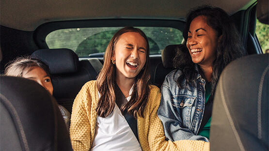 A group of differently aged girls sitting in the backseat of the car laughing with each other 