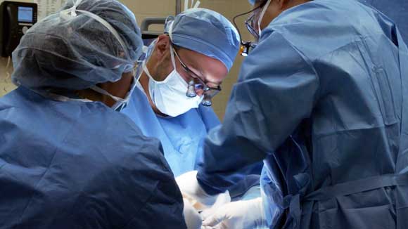 Two surgeons in the hand and upper extremity fellowship perform a surgery, assisted by a surgical nurse.