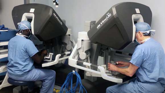 Two surgical critical care fellows, one black and one white, practice using the Da Vinci robotic surgical system.