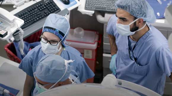 Two vascular surgery residents observe faculty during a surgical procedure.