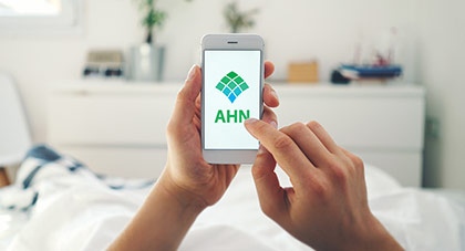 A person's hands holding a phone displaying AHN's website.