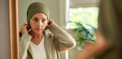 A cancer patient fixing her head covering in a mirror