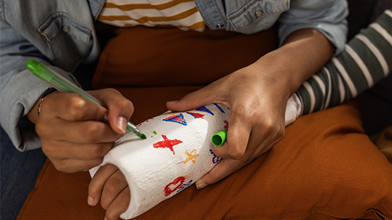 Close up view of young girl's hands signing her brother's cast on his broken arm