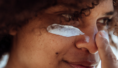Person applying sunscreen to face to protect from sun damage.