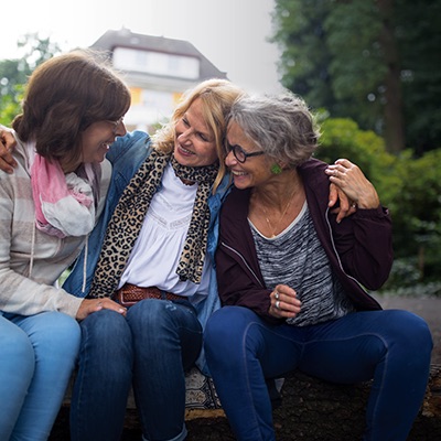 Three women smiling and embracing each other in a park 