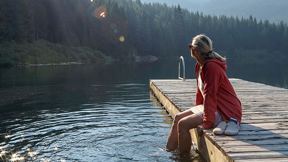 A woman sitting on a dock with her legs in the water.
