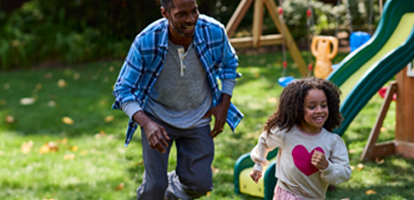 A smiling father playing with his daughter in their backyard