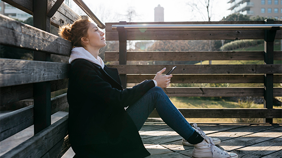 A woman sitting on deck with her phone in her hands contemplating seeking help for intimate partner violence.