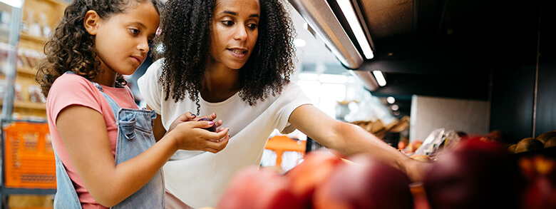 A mother and her young daughter picking fruit from a shelf at a Healthy Food Center