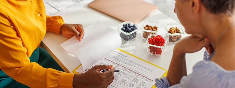 A counselor sitting at a table with a patient showing them a chart, with containers of small fruits and nuts nearby