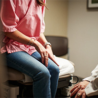 AHN patient sitting on a exam table while talking to a doctor.