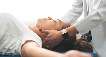 A young woman receives gentle neck treatment from a medical professional in a white coat.