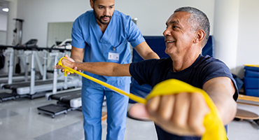 A medical professional assists a man with Parkinson's therapy using resistance bands.